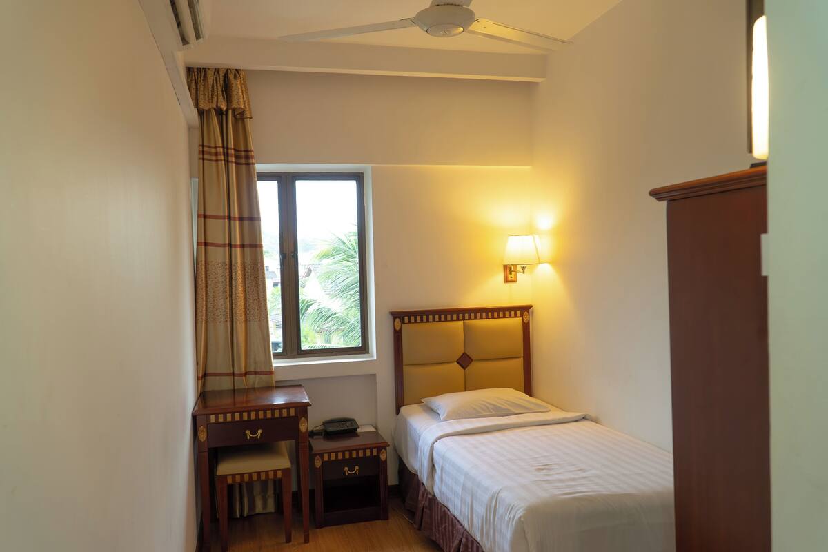 Une chambre à coucher avec un lit, une table de chevet, une lampe et une fenêtre avec des rideaux.