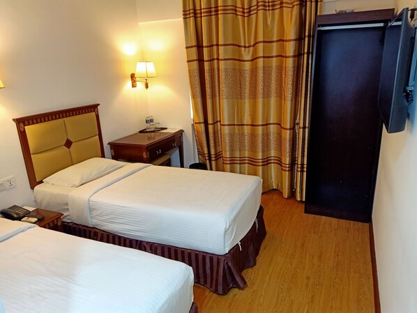 A hotel room with two beds, a nightstand with a lamp, a wooden headboard, a curtain, and a door. - Borneo Suites Hotel (Kota Kinabalu)