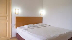Una cama bien tendida con cabecera de madera, dos lámparas fijadas a la pared y una puerta cerrada.