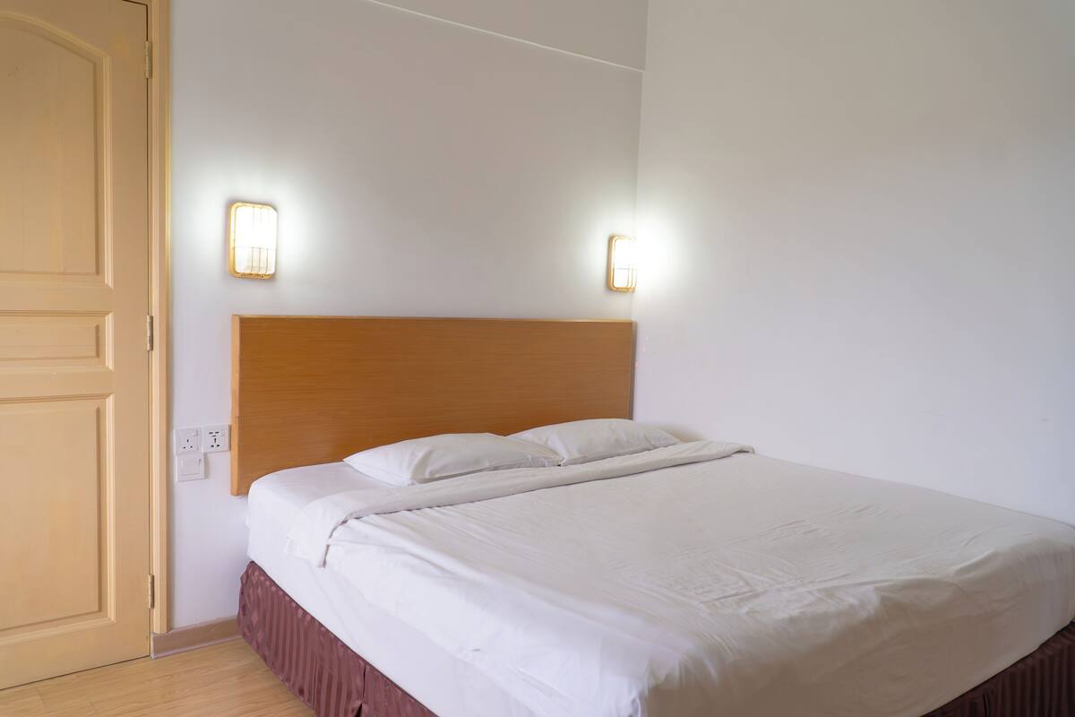Un lit bien fait, avec une tête de lit en bois, deux appliques murales et une porte fermée.