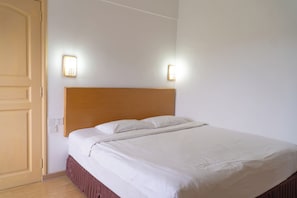 A neatly made bed with a wooden headboard, two wall-mounted light fixtures, and a closed door.