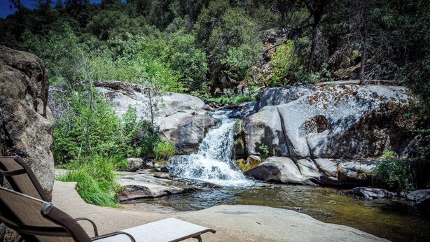 A natural setting with a waterfall, a picnic table, and a bench.