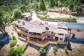 A multi-story wooden house with a balcony, solar panels, and a landscaped yard.