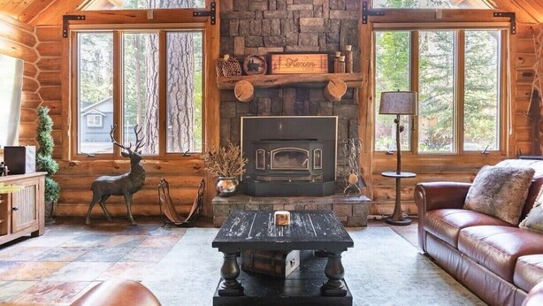 Interior de una cabaña de madera con chimenea de piedra, muebles de madera y una estatua de venado.