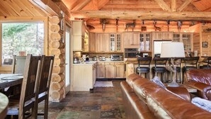 Interior rústico de una cabaña con un comedor de madera, una cocina con armarios de madera y un sofá de cuero.