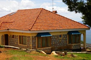 A two-story house with a red-tiled roof, stone walls, and a small porch with blue awnings.