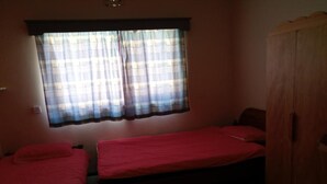 Ein Zimmer mit zwei Einzelbetten, einem Fenster mit kariertem Vorhang und einem Holzschrank.