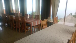Ein Essbereich mit einem langen Tisch und Stühlen, großen Fenstern mit Vorhängen und Blick auf das Meer.