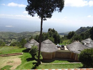 A view of thatched-roof huts with a grassy landscape and distant hills. - Kilima Resort (Iten)