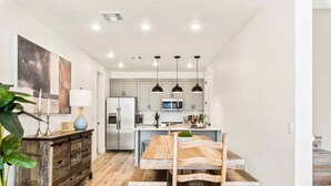 Une cuisine moderne avec des meubles blancs, un réfrigérateur en acier inoxydable et une table à manger en bois, accompagnée de bancs.
