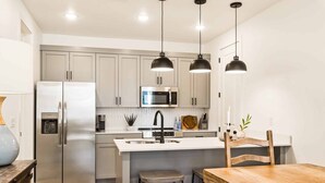 Une cuisine moderne dotée d’appareils électroménagers en acier inoxydable, d’un îlot central avec des tabourets et d’un éclairage suspendu.