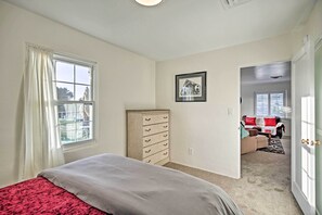 Un dormitorio con cama, cómoda, cuadro en la pared y vista a otra habitación con sofá y ventana.