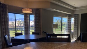 A spacious room with a large dining table, a seating area, and large windows offering a view of a golf course and mountains.