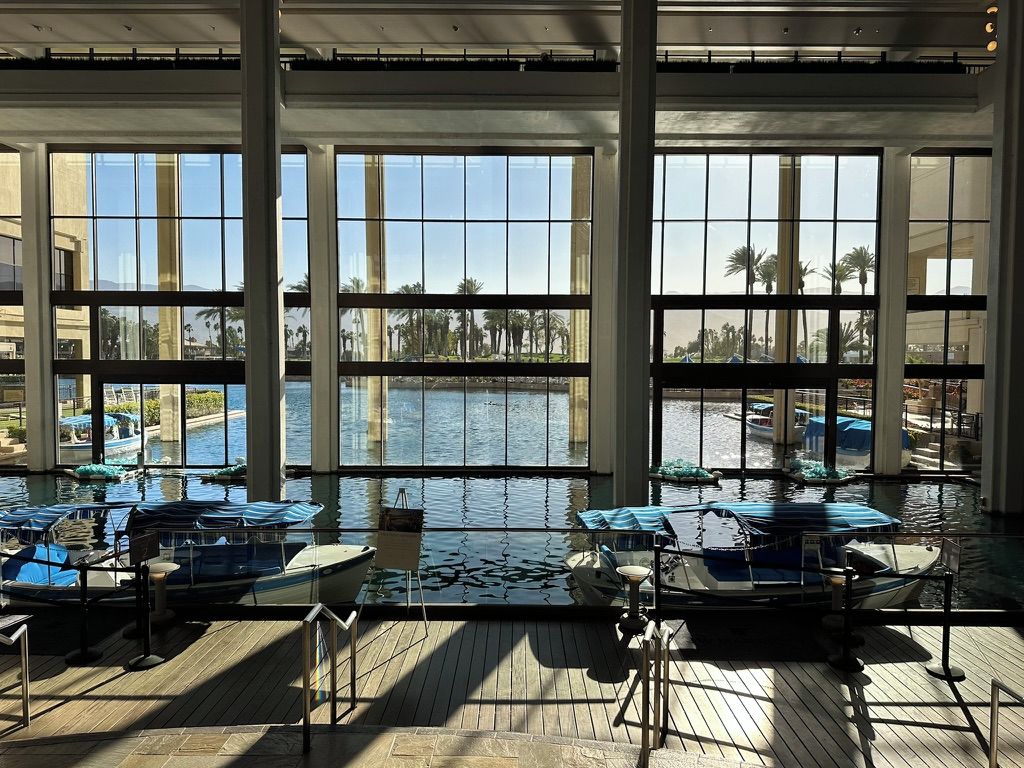 A large indoor pool with clear views of palm trees and boats outside.