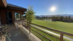 A balcony with a view of a golf course, a tree, and a mountain range in the background.