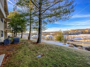 Ett bostadsområde med ett stort träd i förgrunden, en byggnad med en balkong på vänster sida och en utsikt över ett område med flera hus och en parkeringsplats i bakgrunden.