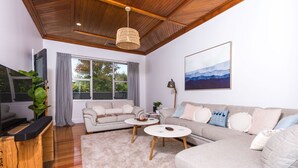 Ein modernes Wohnzimmer mit Holzbalkendecke, einem grauen Sofa, einem beigen Sofa, einem Couchtisch und einem Fernsehschrank.