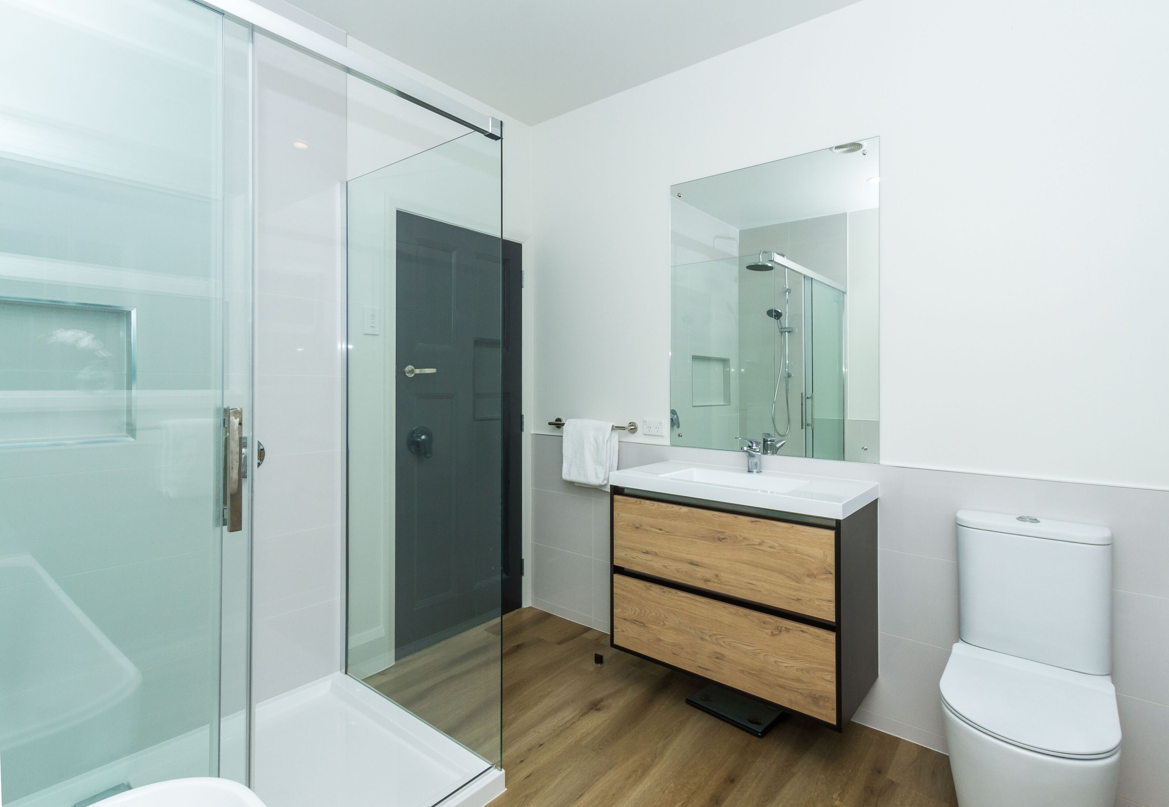 Een moderne badkamer met een douchecabine van glas, een houten wastafelmeubel met een witte wastafel en een wit toilet.