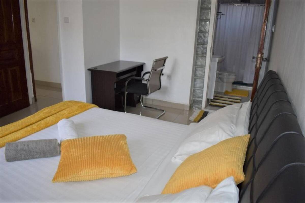A hotel room with a bed, a desk, and a bathroom visible through a glass door.