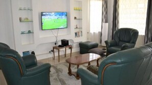 A living room with teal leather sofas, a wooden coffee table, and a flat-screen TV mounted on the wall. - North Manor Nakuru (Nakuru)