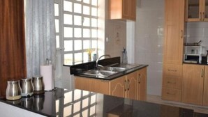 A modern kitchen with a black countertop, stainless steel sink, wooden cabinets, and a window with blinds. - North Manor Nakuru (Nakuru)