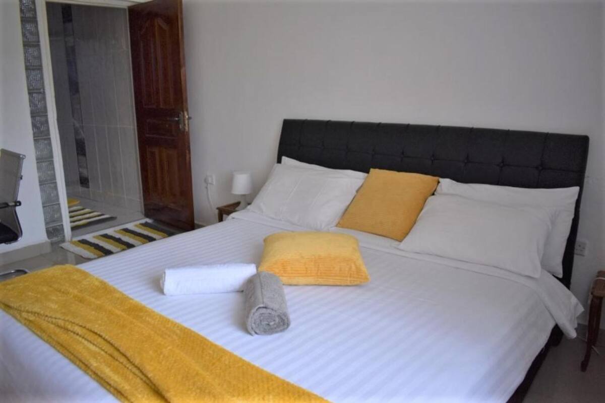 A hotel room with a bed, a wooden door, and a white wall.