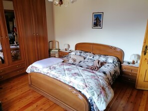 A wooden bed with a floral bedspread, a nightstand with a lamp, and a wardrobe with a mirror. - Chalet of the enchanted country (Moncenisio)