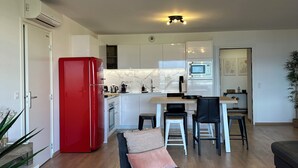 Eine moderne Küche mit weißen Schränken, einem roten Kühlschrank und einem Essbereich mit einem schwarzen Stuhl und einem Holztisch.