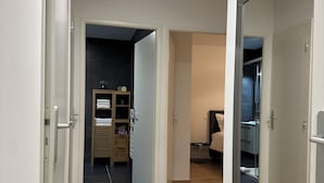 Ein Flur mit Holzboden, einer spiegelnden Schranktür und einem Zimmer mit Bett und Nachttisch.