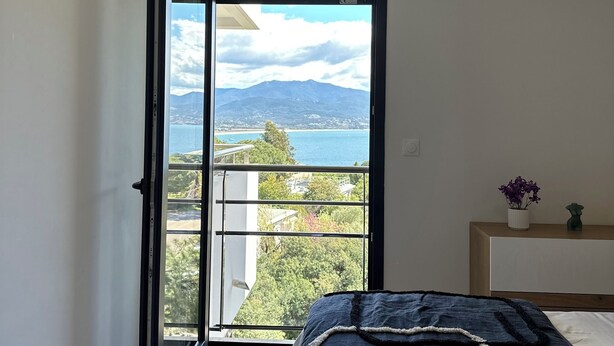 Ein Schlafzimmer mit einer großen Schiebetür, die auf einen Balkon mit herrlichem Blick auf Berge und ein Gewässer führt.