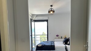 Ein Schlafzimmer mit Bett, Schreibtisch und Stuhl. Ein Fenster bietet Blick auf Grünfläche.