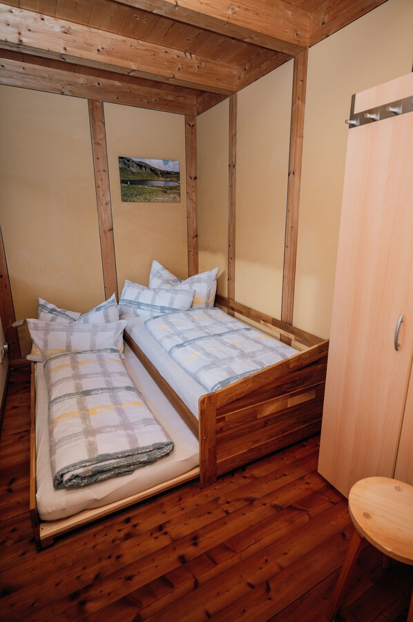 A small, wooden-framed room with two single beds, a wooden floor, and a small wooden table.