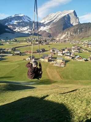 A person on a swing overlooking a village with mountains in the background. - Vacation cottage FuchsbAU, Austria (Au)