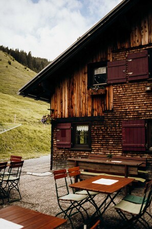 A rustic wooden building with a balcony, outdoor seating, and a grassy hillside in the background. - Vacation cottage FuchsbAU, Austria (Au)