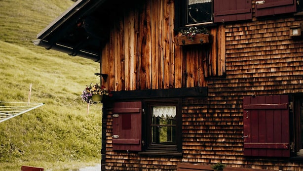 A rustic wooden building with a balcony, outdoor seating, and a grassy hillside in the background. - Vacation cottage FuchsbAU, Austria (Au)
