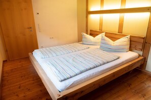A wooden bed with striped bedding in a room with wooden flooring and a wooden headboard. - Vacation cottage FuchsbAU, Austria (Au)