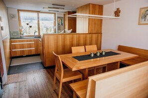 A compact kitchen with wooden cabinets, a dining table with chairs, and a window with a view of greenery. - Vacation cottage FuchsbAU, Austria (Au)