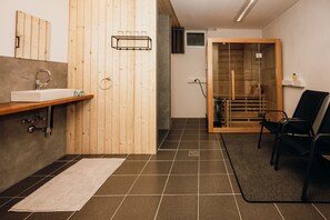 A modern bathroom with a wooden vanity, a sink, and a glass shower enclosure. - Vacation cottage FuchsbAU, Austria (Au)