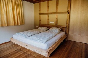 A wooden-framed bed with a mattress and pillows, a wooden floor, and a window with curtains. - FuchsbAU Vacation Cabin, Austria (Au)