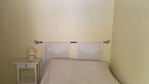 Ein kleines, schlichtes Zimmer mit einem Bett, einem Nachttisch und einer Lampe.