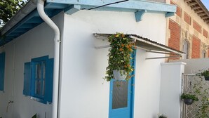 Ein weißes Gebäude mit blauer Tür und Fensterläden, umgeben von Blumentöpfen und einem kleinen Garten.