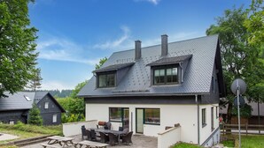 A two-story house with a sloped roof, a patio with a table and chairs, and a small garden area. - Rennsteig Trail Family Escape (Eisfeld)