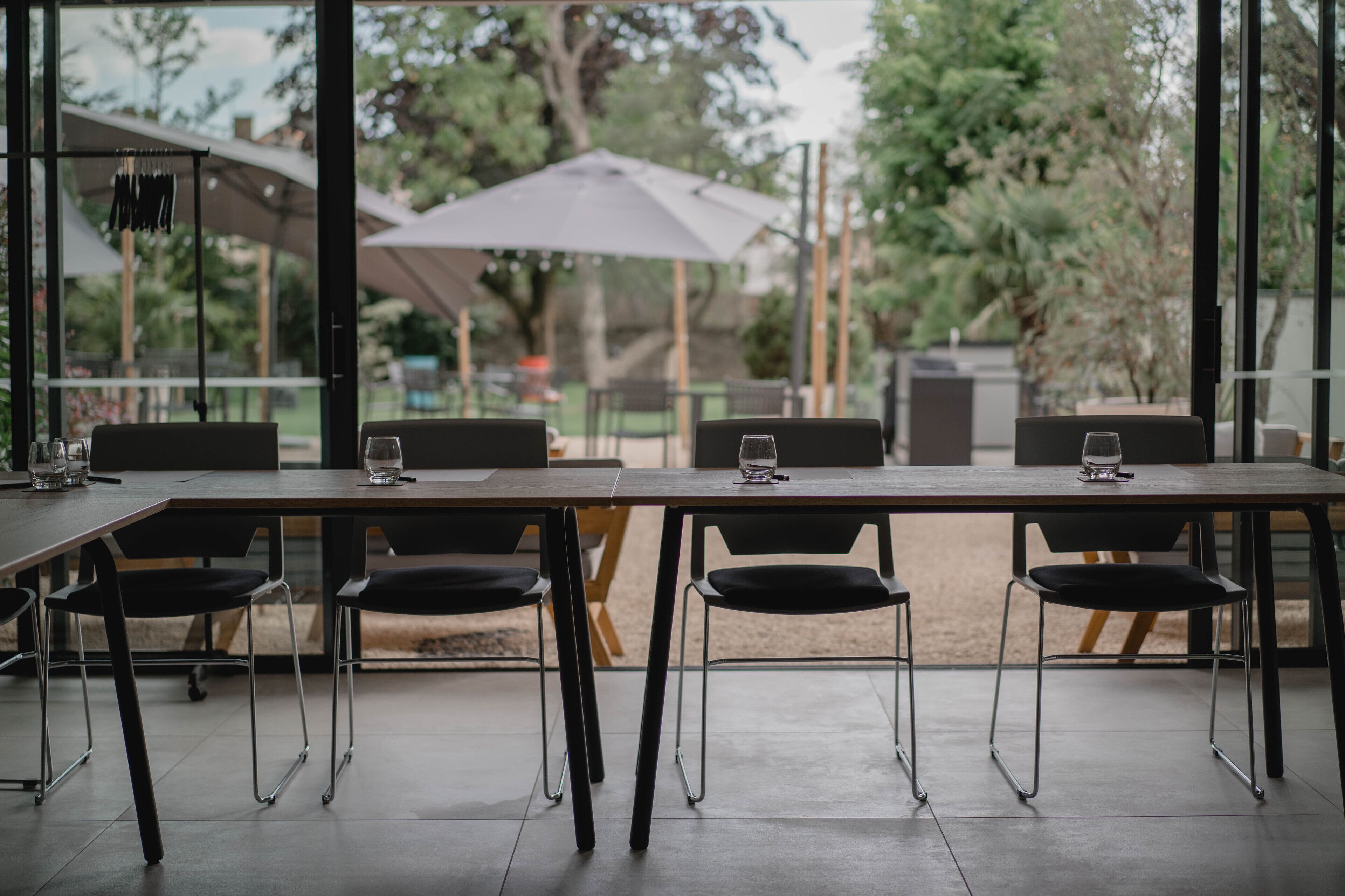 Un espace de restauration extérieur moderne, doté d’une longue table et de chaises, de grands parasols et offrant une vue sur les arbres et la verdure.