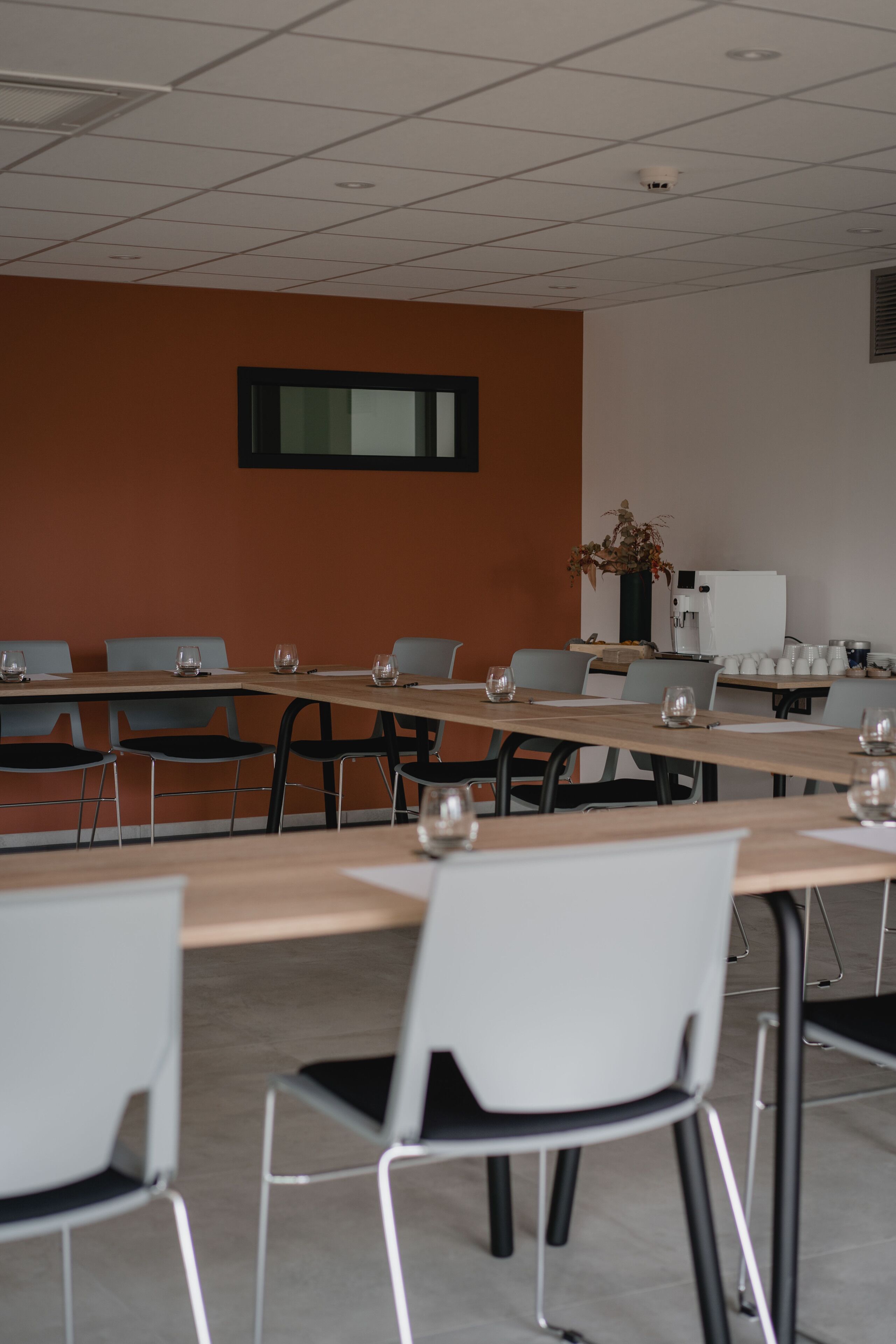 Un salón de conferencias con mesas y sillas, una máquina de café y una planta en la pared.