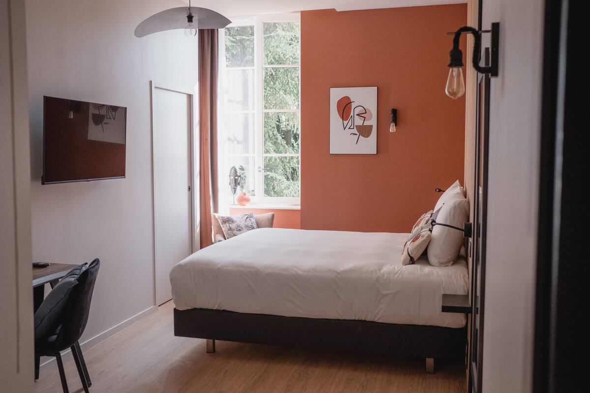 A bedroom with a bed, a desk, and a window.