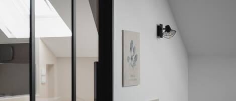 A modern interior with a skylight, a wall-mounted lamp, and framed botanical prints.