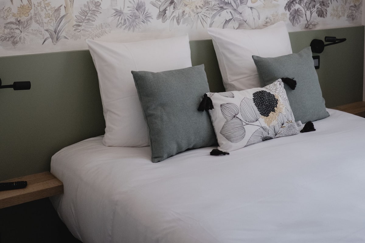 A bedroom with a bed, pillows, and a wall with a tropical plant wallpaper.