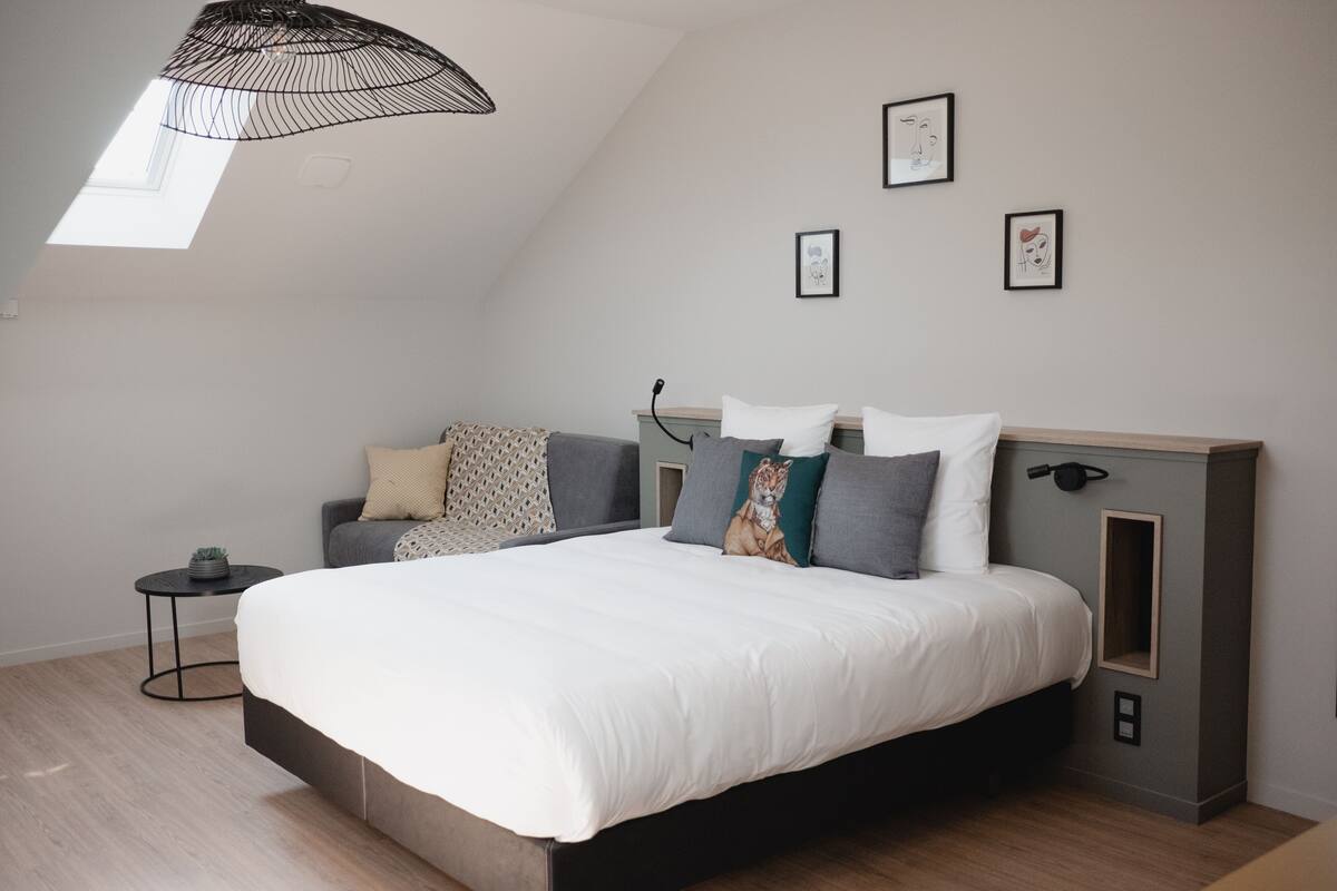 A modern bedroom with a large bed, a side table, a small round table, and a ceiling light fixture.