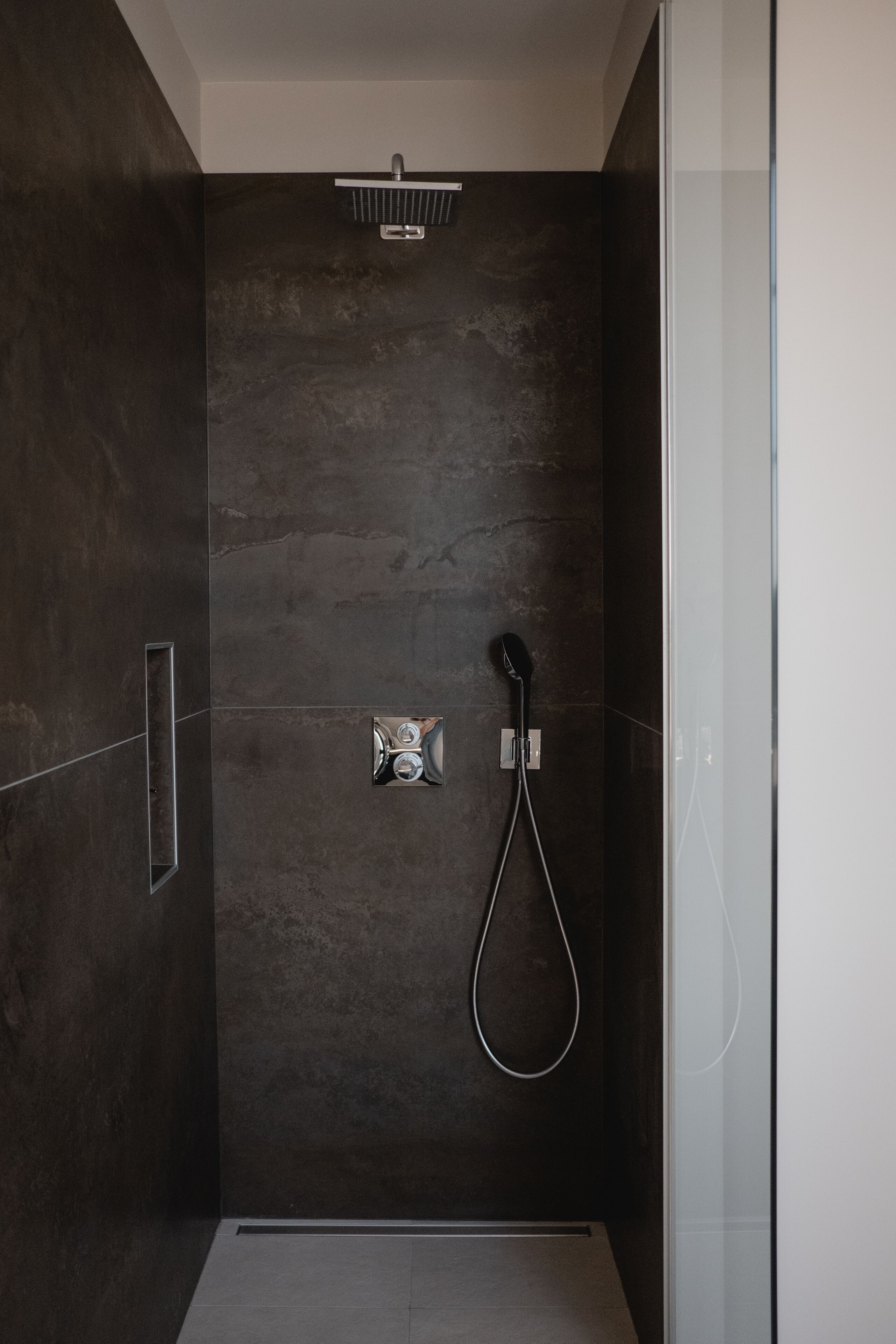 Una ducha moderna con cabina de vidrio, cabezal de ducha manual y panel de control en la pared.