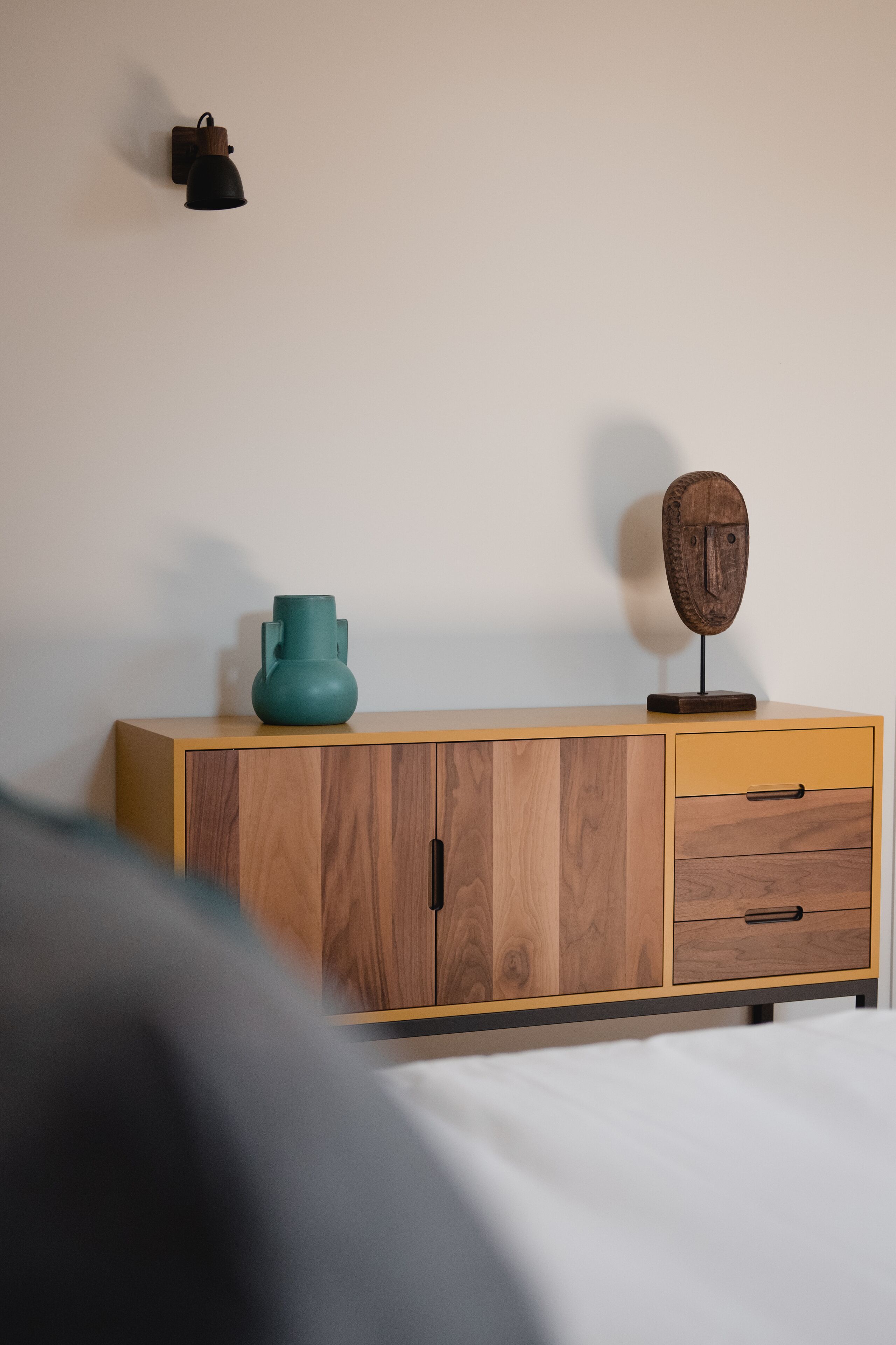 A wooden cabinet with two drawers and a teal vase on top.